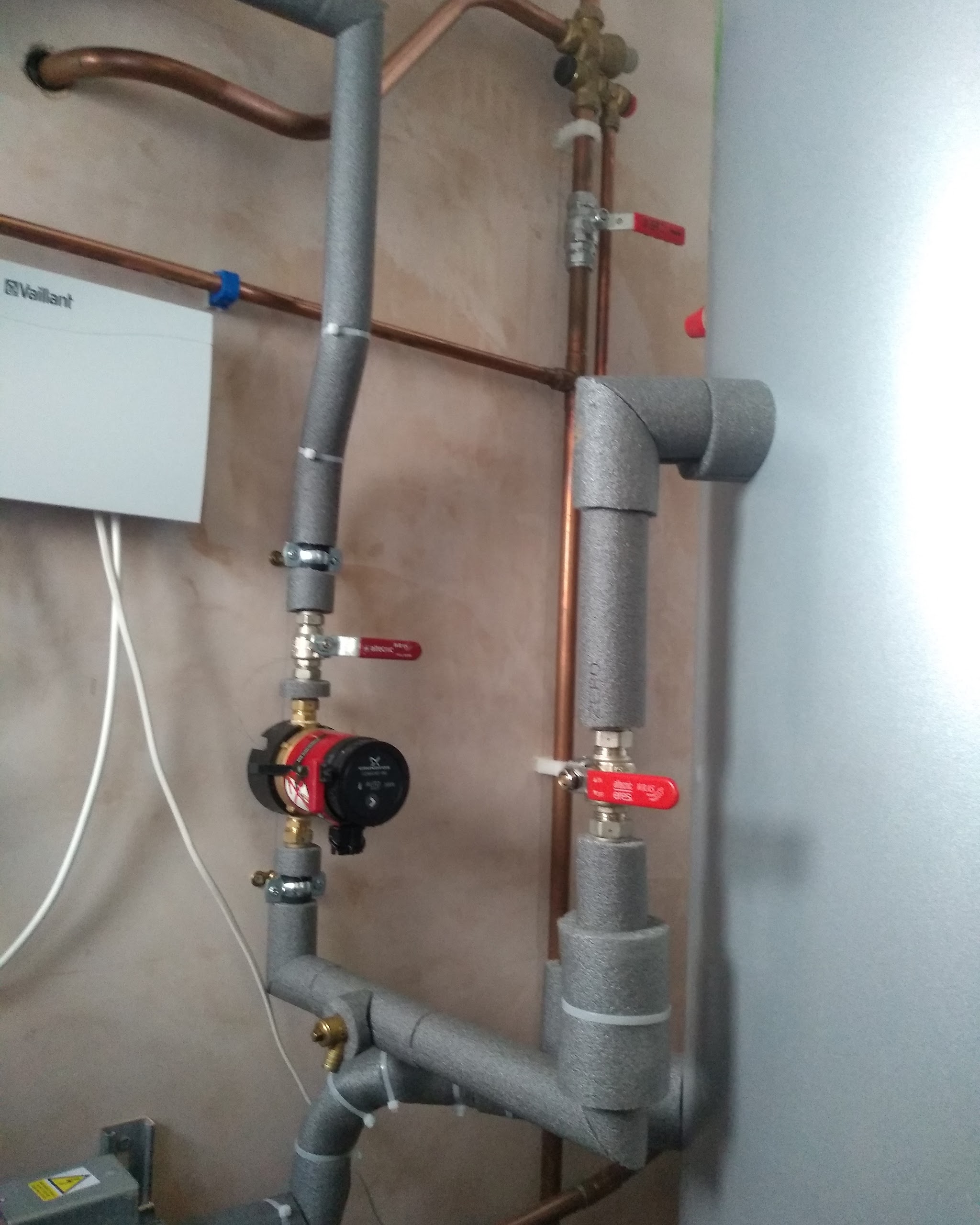 Neat insulated pipework, pump and valves beside an unvented hot water cylinder